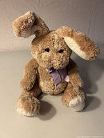 Front view of light brown plush bunny with purple ribbon