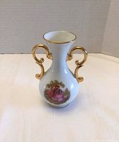 Front view of white porcelain vase showing hand-painted scene and gilt handles