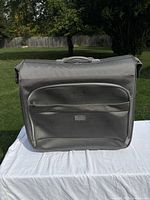 Front view of gray rolling garment bag showing front pocket and logo tag