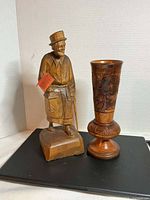 Both items side by side on black surface: carved figurine and turned wood vase