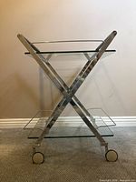 Full side view of chrome X-frame bar cart showing two glass shelves and casters