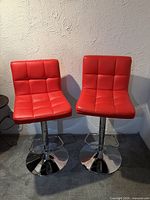 Front view of both red bar stools on chrome bases