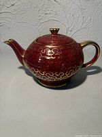 Left profile of burgundy porcelain teapot showing gold scroll pattern, handle and spout