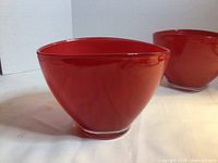 Side view of one red glass bowl with clear foot, second bowl partly visible