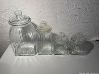 Four ribbed clear glass canisters with lids side by side showing size gradation