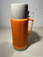 Front view of orange and white Thermos flask with handle