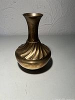 Front view of brass vase showing swirl fluted design and patina