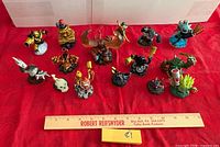 All 18 Skylanders figures arranged on red cloth with ruler for scale