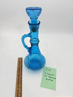 Full view of blue glass bottle with stopper beside ruler