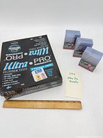 Box of Ultra Pro Platinum hologram 3-pocket pages with three packs of 3"x4" super thick toploaders displayed next to ruler for scale
