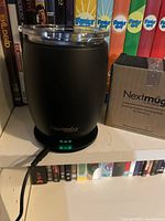 Mug seated on charging coaster, power indicator lit, boxed spare coaster visible