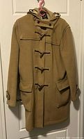 Front view of camel duffle coat on hanger showing overall design, closures, pockets, hood