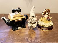 Full lot view showing ceramic sewing machine teapot, resin gnome, and girl figurine