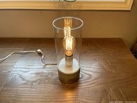 Lamp illuminated showing glass cylinder and silver leaf concrete base