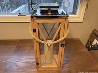 Front view of wood and glass lantern with rope handle and faux candle inside