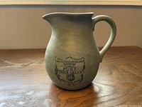 Front view of green ceramic jug displaying dairy stamp graphic