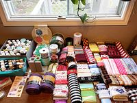 Overall view of ribbon rolls, paint bottles, bow maker and wood clock kit on table
