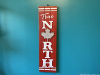 Front view of red wood sign showing "True NORTH" text and maple leaf