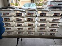 Front view showing 25 stacked clear bins with white lids on table