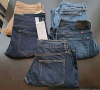 Stack of five jeans showing variety including tan pair