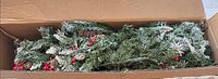 Box with packed artificial tree sections showing green snow-dusted branches with berries