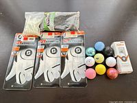 Lot overview showing three FootJoy gloves, package of black tees, bag of glow tees, assorted colored golf balls, and Titleist Velocity sleeve