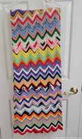 Full view of folded multicolor chevron afghan hanging on hanger