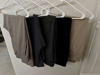Five pairs of dress pants hanging side-by-side showing color range