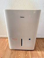 Front view of white Midea dehumidifier showing water-level window