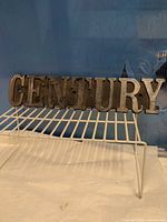 Front view of plaster plaque showing raised "CENTURY" letters and metallic finish