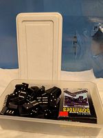 Domino tiles in white plastic container with lid and cardboard sleeve visible