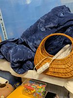 Blue plush blanket, wicker handbag, power strip, clear toy box visible