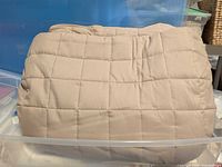 Front view of folded beige quilted duvet in clear tote