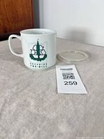 Mug front view with Greening the Hill logo, rubber lid beside