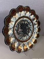 Front view showing silver-gold iridescence, scalloped rim and grape motif