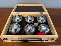 Open wooden case showing six chrome boules, wooden jack, red marker