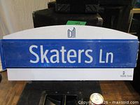 Front view of Skaters Ln street sign showing text, colour scheme, shape