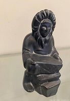 Front view of dark ceramic Inuit figure statue seated and holding slab