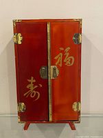 Full front view of red lacquer jewelry cabinet showing doors, hardware and feet