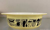 Side view showing full casserole dish with yellow exterior and black food motif graphics