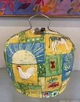 Front view of tea cozy showing farm motif fabric and metal handle