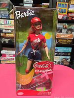 Front view of boxed Barbie Coca-Cola Special Edition doll with helmet and accessories visible