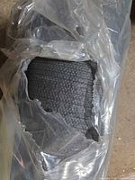 Close-up of torn plastic showing carpet texture and dark gray color