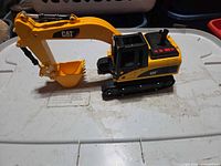 Left side view of CAT plastic excavator toy on lid, showing full vehicle