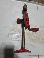 Side view showing red gear wheel, wood handles, steel shaft, red base