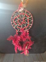 Full view of red dreamcatcher hanging against dark background
