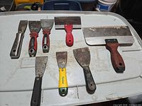 Eight assorted putty knives and scrapers laid out showing variety and condition