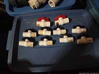 Ten white PVC ball valves with mixed red and black wing handles laid out