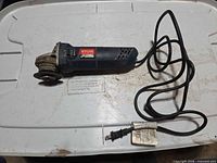 Full view of Ryobi angle grinder with cord on white surface