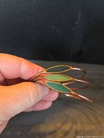 Hand holding three thin copper bangles showing enamel navette inlays